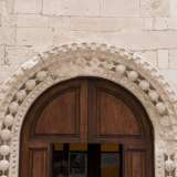 Il piccolo portale in legno � inserito in una perimetro decorativo di spessi grani di rosario in pietra, incastonato in una doppia cornice dentellata